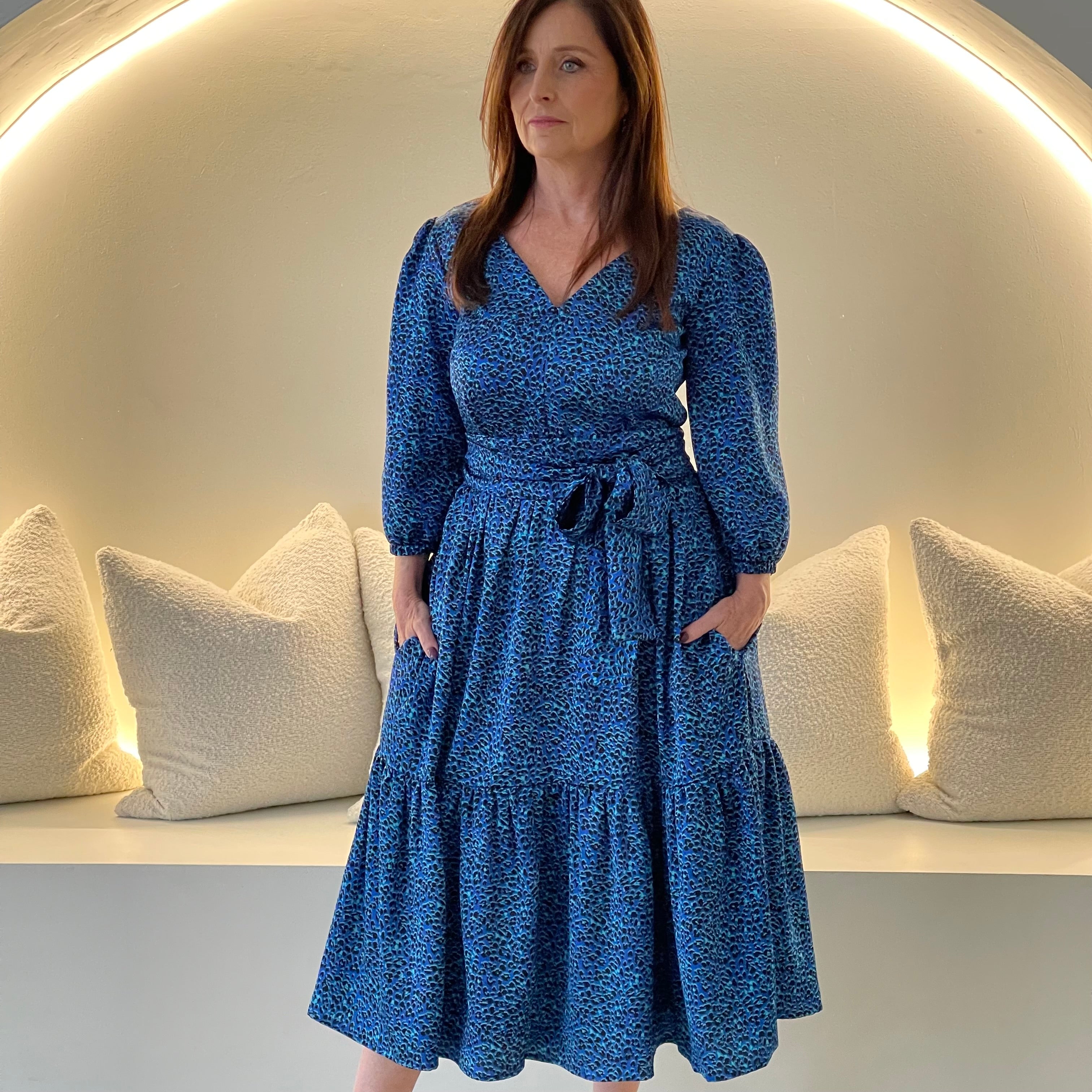 Sapphire background with a deep teal and black very discreet and discerning animal print. V-neck. Gathered sleeve at the shoulder. Roomy Sleeves that can be worn at long sleeves or three quarters. Cuffed at the wrist with discreet elastic threaded through. 7/8s in length. Two tier skirt. Lower tier with a subtle ruffle. Fitted at the waist with elastic threaded through the back discreetly for comfort and ease of getting on. Sash worn on waist. Centre back zipper.