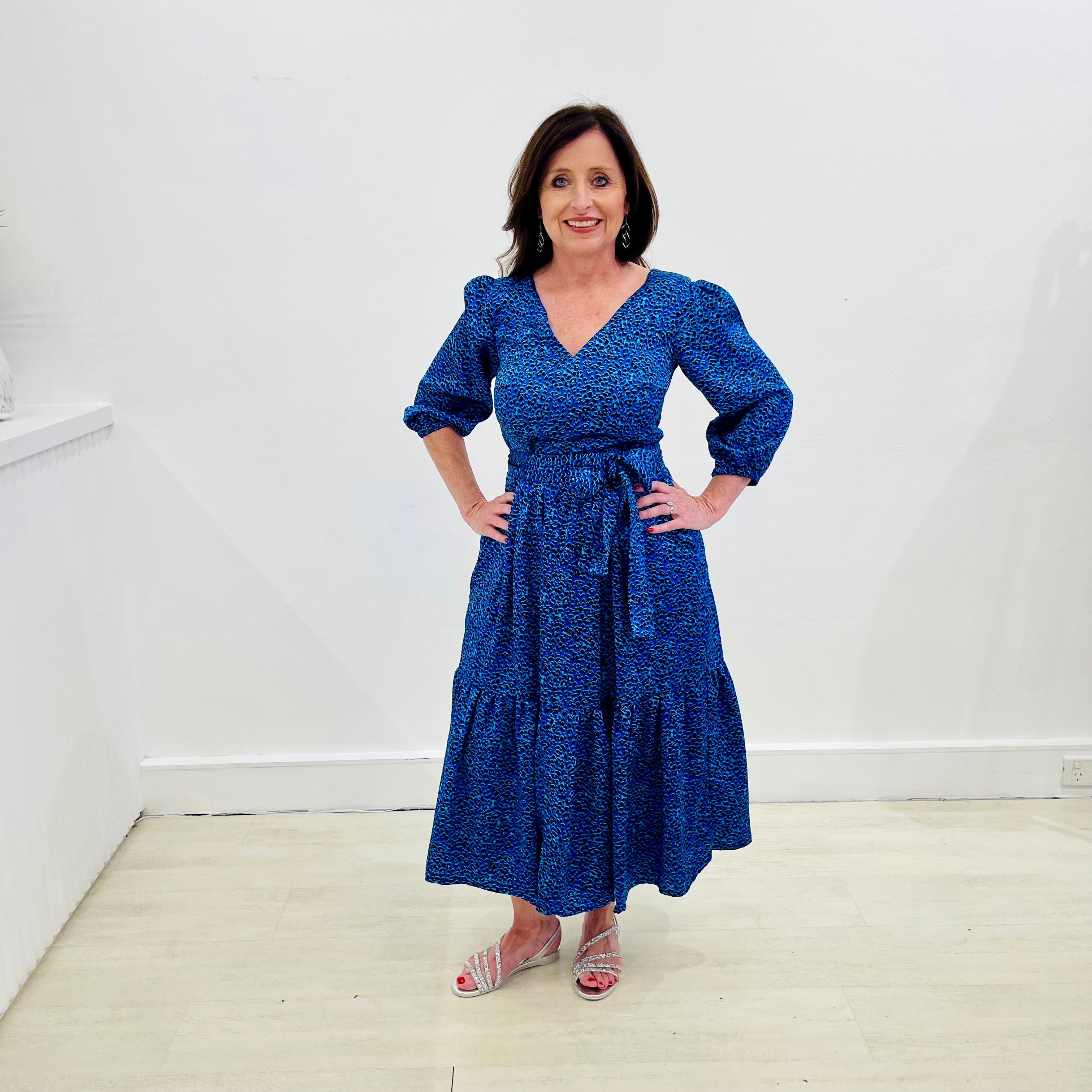 Sapphire background with a deep teal and black very discreet and discerning animal print. V-neck. Gathered sleeve at the shoulder. Roomy Sleeves that can be worn at long sleeves or three quarters. Cuffed at the wrist with discreet elastic threaded through. 7/8s in length. Two tier skirt. Lower tier with a subtle ruffle. Fitted at the waist with elastic threaded through the back discreetly for comfort and ease of getting on. Sash worn on waist. Centre back zipper.