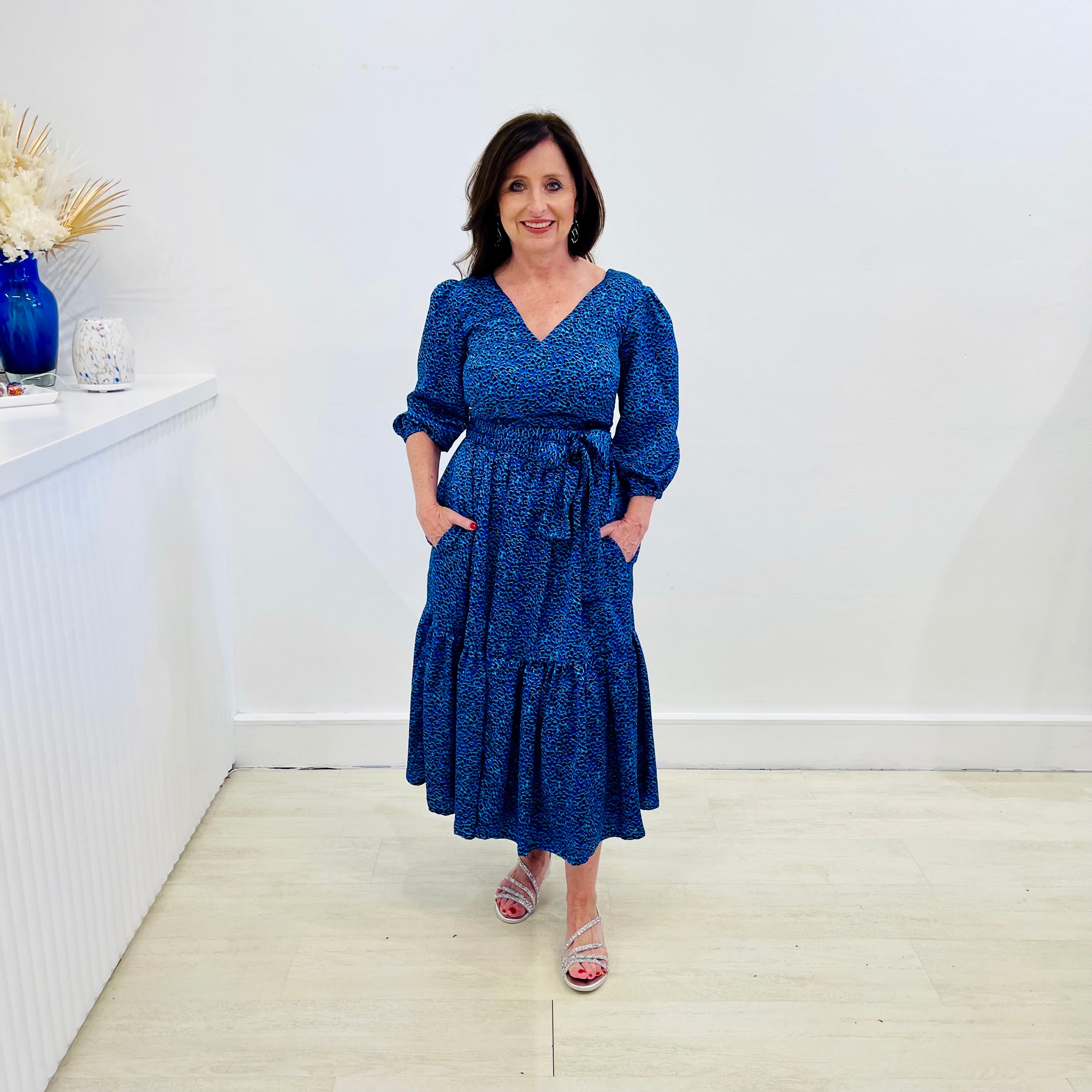 Sapphire background with a deep teal and black very discreet and discerning animal print. V-neck. Gathered sleeve at the shoulder. Roomy Sleeves that can be worn at long sleeves or three quarters. Cuffed at the wrist with discreet elastic threaded through. 7/8s in length. Two tier skirt. Lower tier with a subtle ruffle. Fitted at the waist with elastic threaded through the back discreetly for comfort and ease of getting on. Sash worn on waist. Centre back zipper.