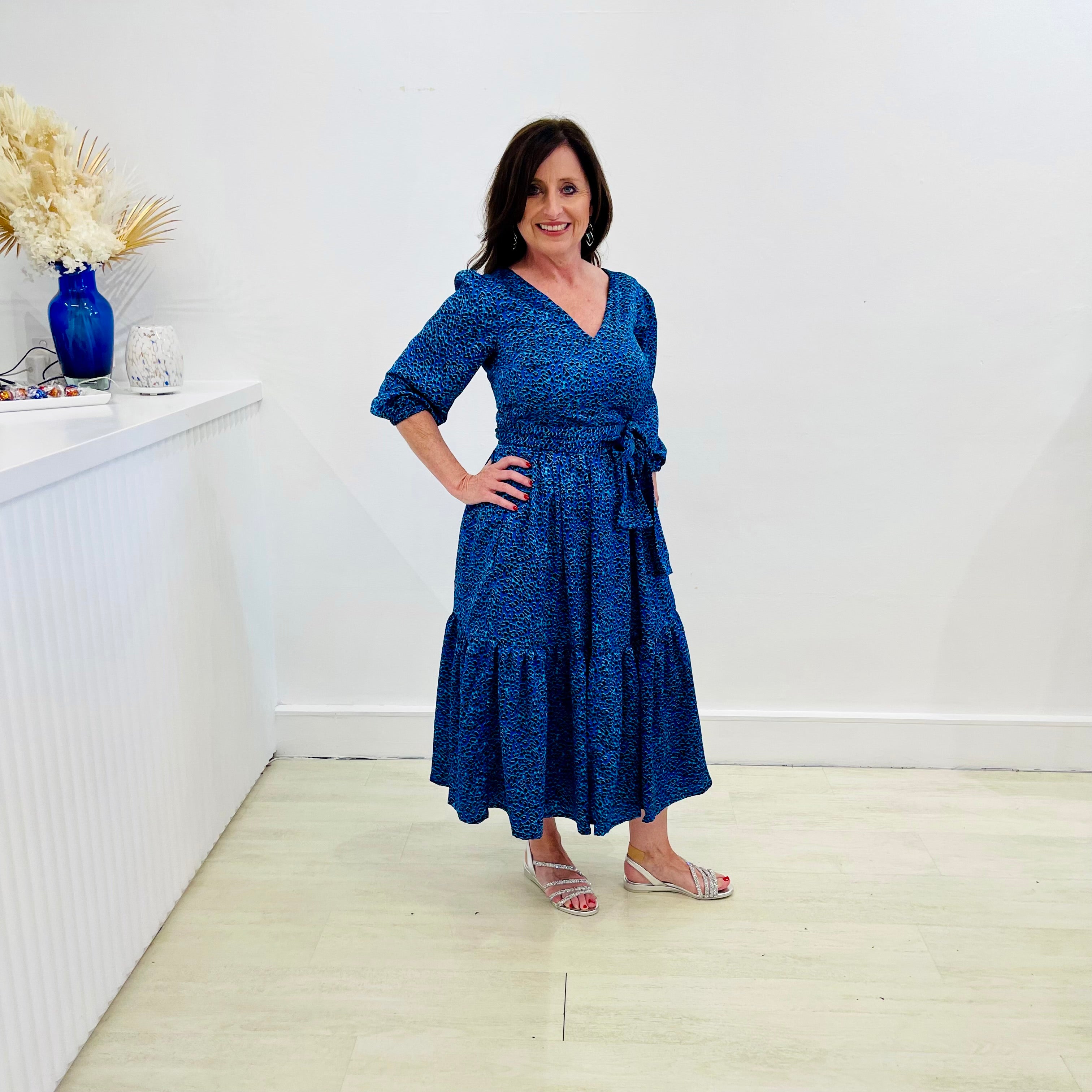 Sapphire background with a deep teal and black very discreet and discerning animal print. V-neck. Gathered sleeve at the shoulder. Roomy Sleeves that can be worn at long sleeves or three quarters. Cuffed at the wrist with discreet elastic threaded through. 7/8s in length. Two tier skirt. Lower tier with a subtle ruffle. Fitted at the waist with elastic threaded through the back discreetly for comfort and ease of getting on. Sash worn on waist. Centre back zipper.