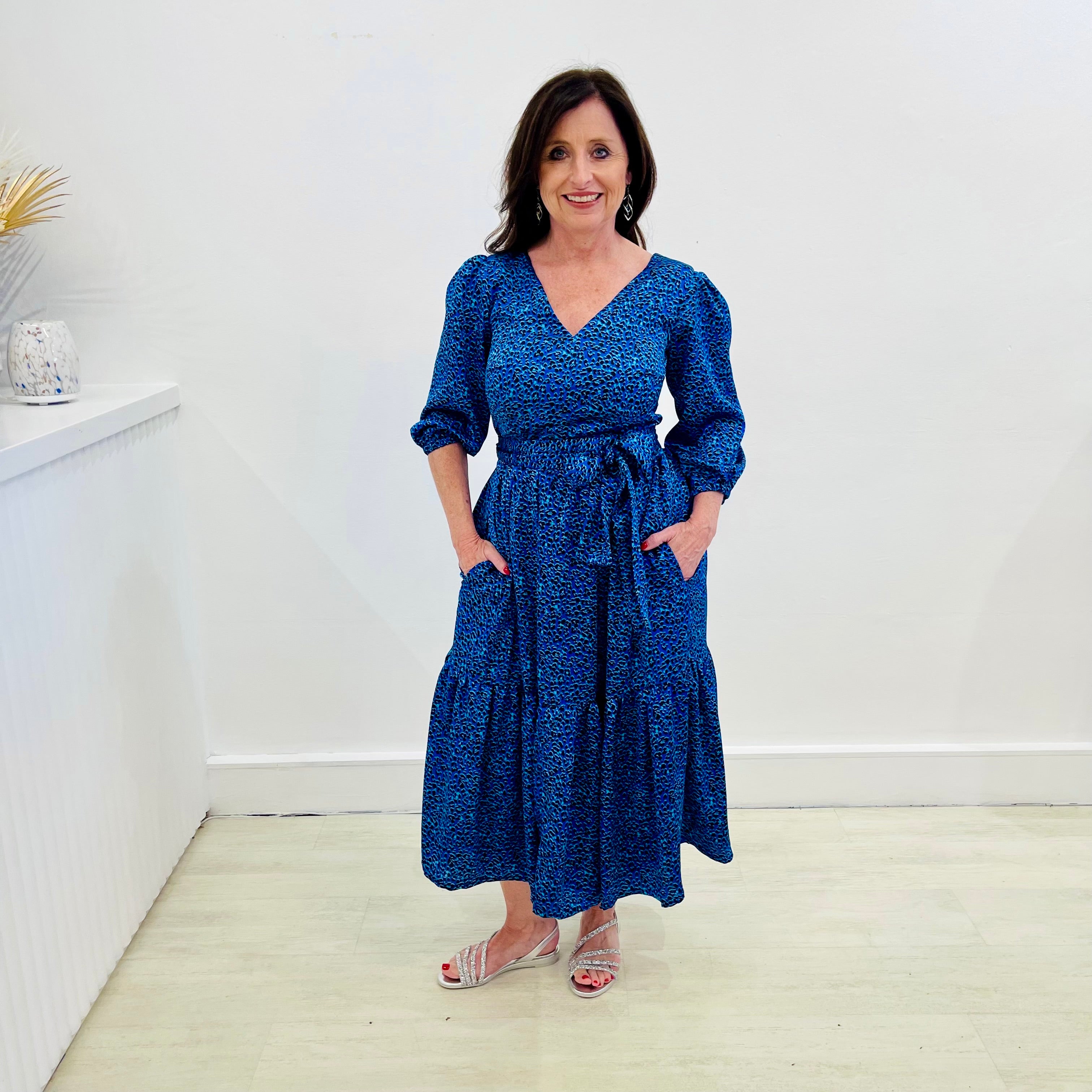 Sapphire background with a deep teal and black very discreet and discerning animal print. V-neck. Gathered sleeve at the shoulder. Roomy Sleeves that can be worn at long sleeves or three quarters. Cuffed at the wrist with discreet elastic threaded through. 7/8s in length. Two tier skirt. Lower tier with a subtle ruffle. Fitted at the waist with elastic threaded through the back discreetly for comfort and ease of getting on. Sash worn on waist. Centre back zipper.