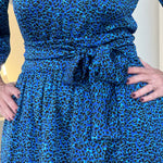 Sapphire background with a deep teal and black very discreet and discerning animal print. V-neck. Gathered sleeve at the shoulder. Roomy Sleeves that can be worn at long sleeves or three quarters. Cuffed at the wrist with discreet elastic threaded through. 7/8s in length. Two tier skirt. Lower tier with a subtle ruffle. Fitted at the waist with elastic threaded through the back discreetly for comfort and ease of getting on. Sash worn on waist. Centre back zipper.