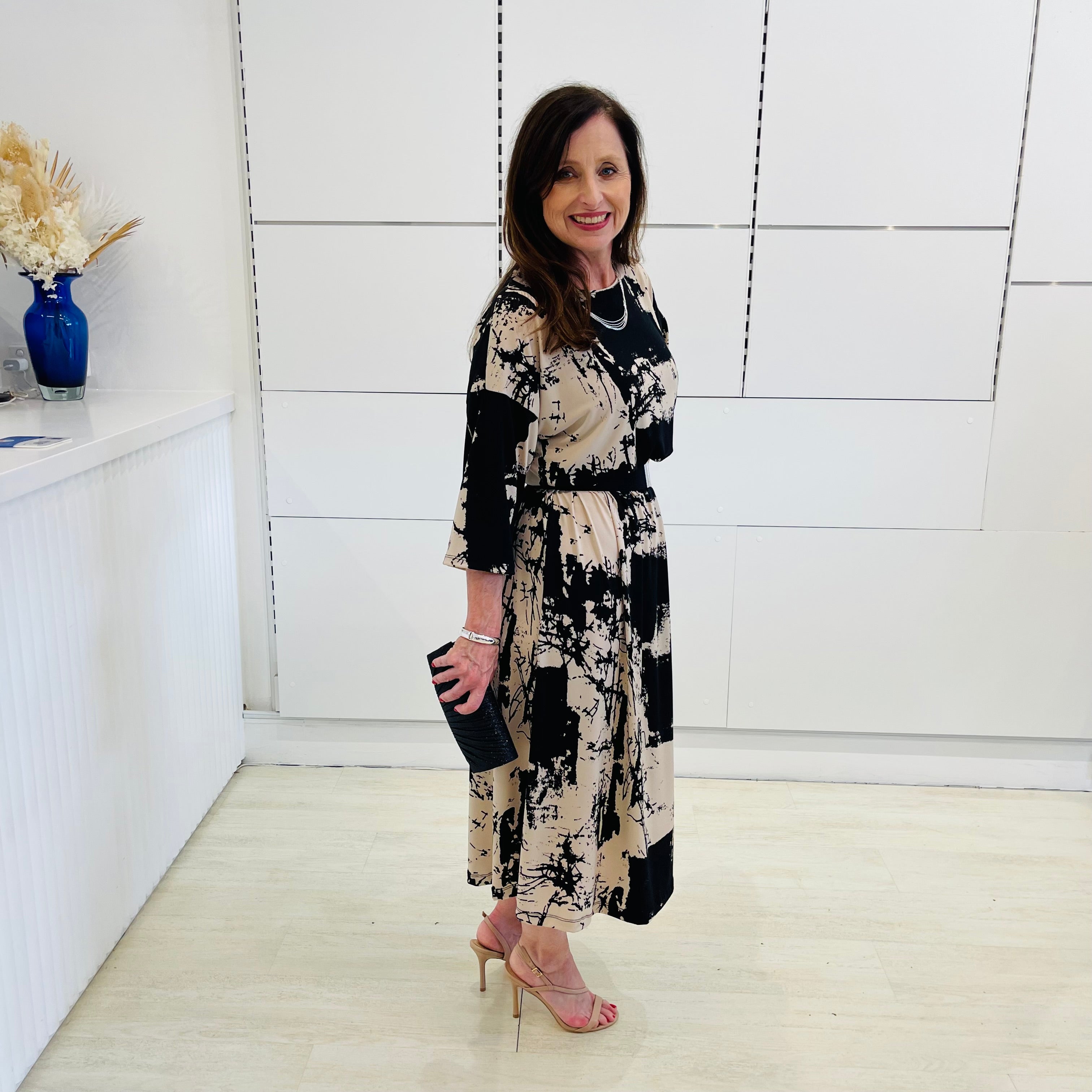 Black and beige print, 3/4 sleeve, midi length dress for special event wear. Relaxed fit dress. With black clutch bag.