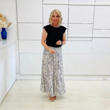 Woman wearing a black top and floral skirt in a minimalistic room.