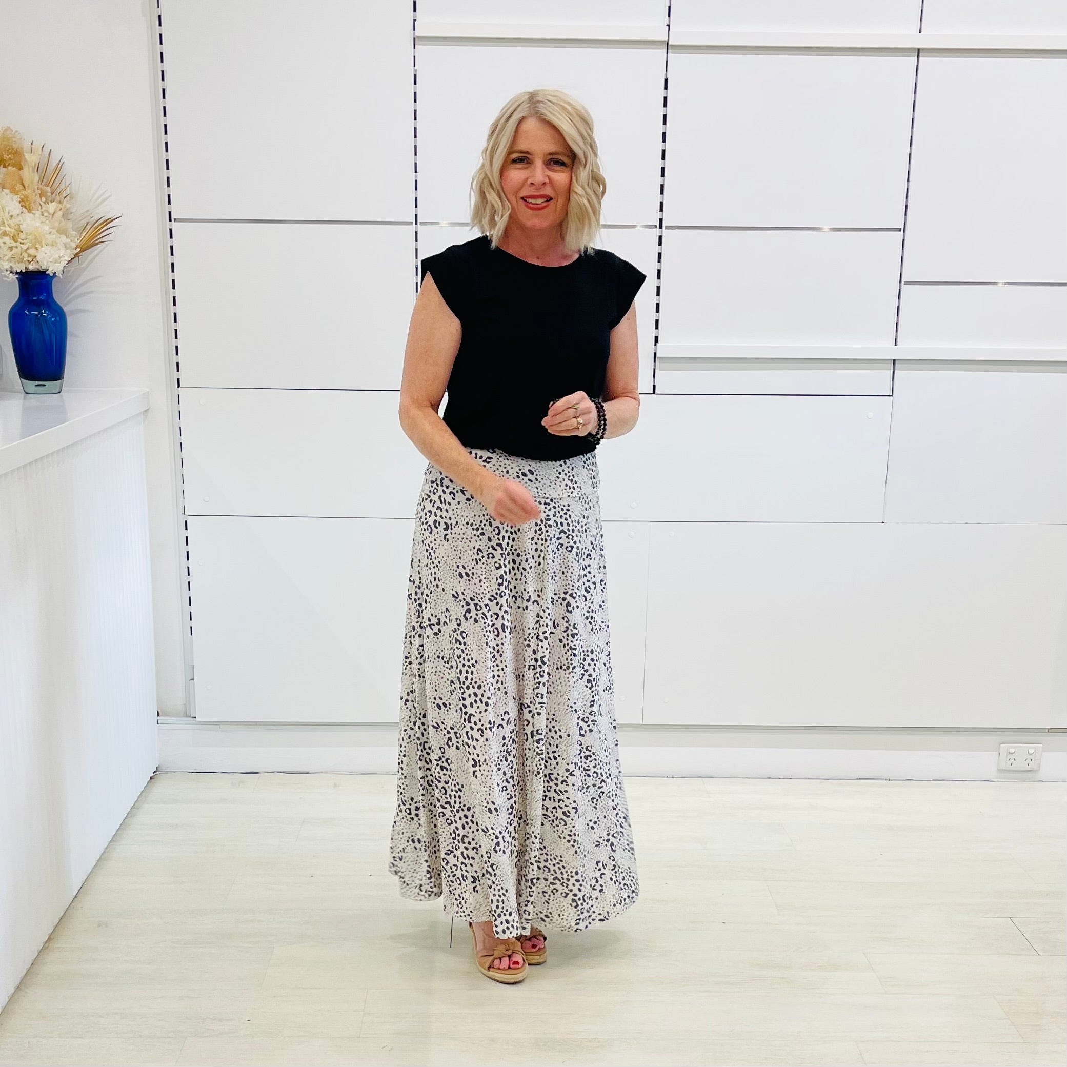 Woman wearing a black top and floral skirt in a minimalistic room.
