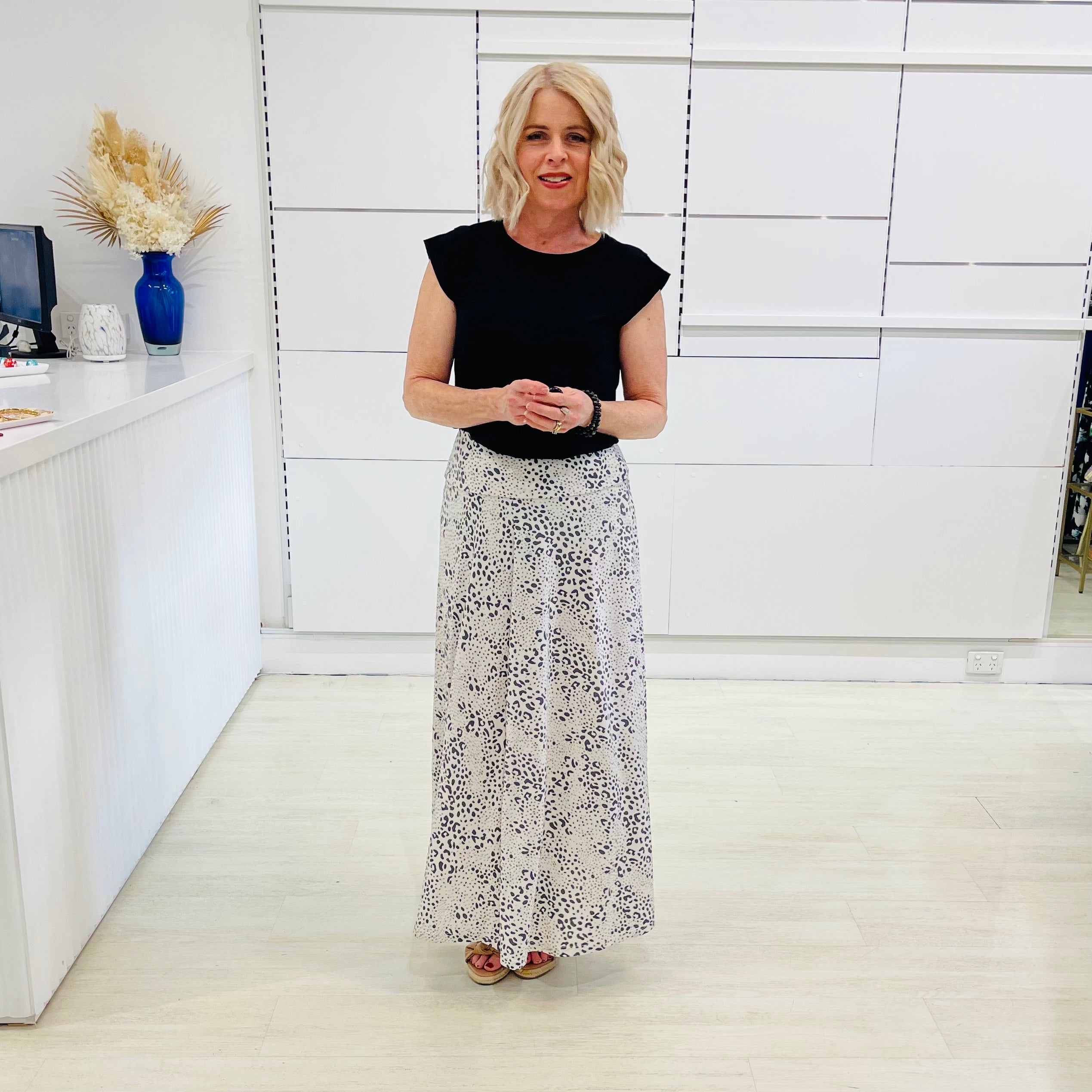Woman in black top and patterned skirt standing in a modern interior setting.