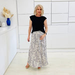 Woman wearing a black top and patterned skirt in a minimalistic room.