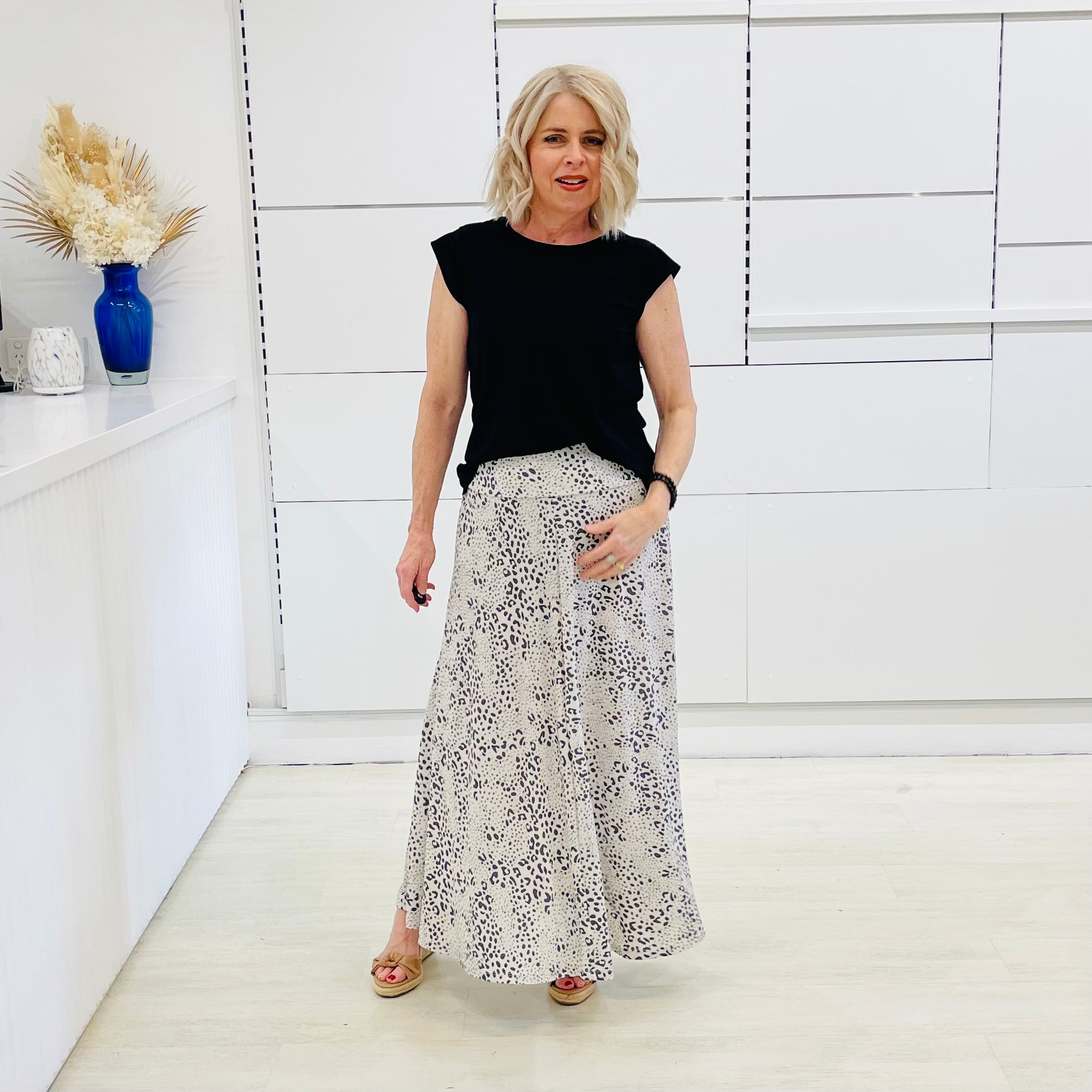 Woman wearing a black top and patterned skirt in a minimalistic room.