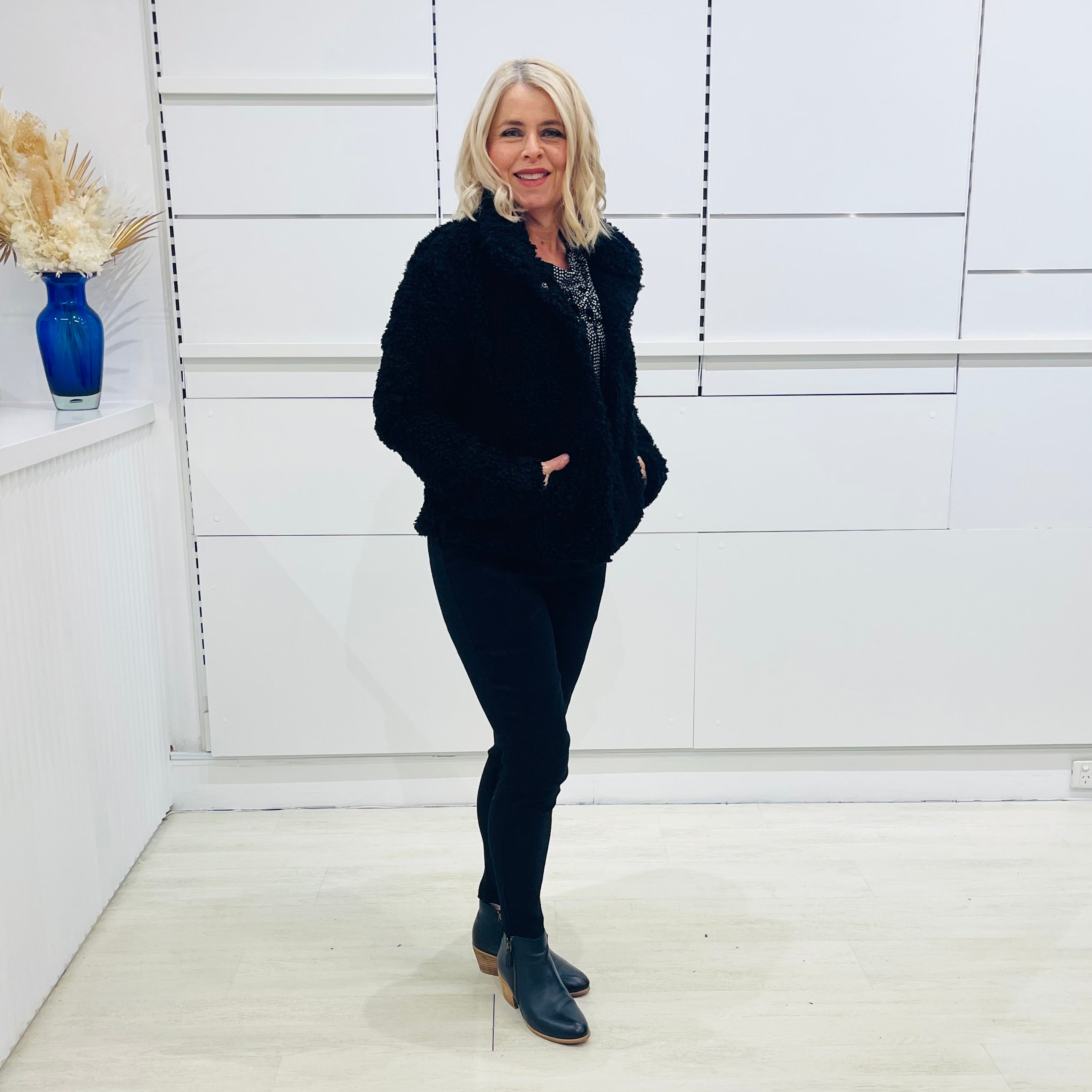 Black fluffy, faux fur, teddy bear jacket with pockets. Worn with black tailored fitted pants and a black and silver sparkly cowl neckline top.