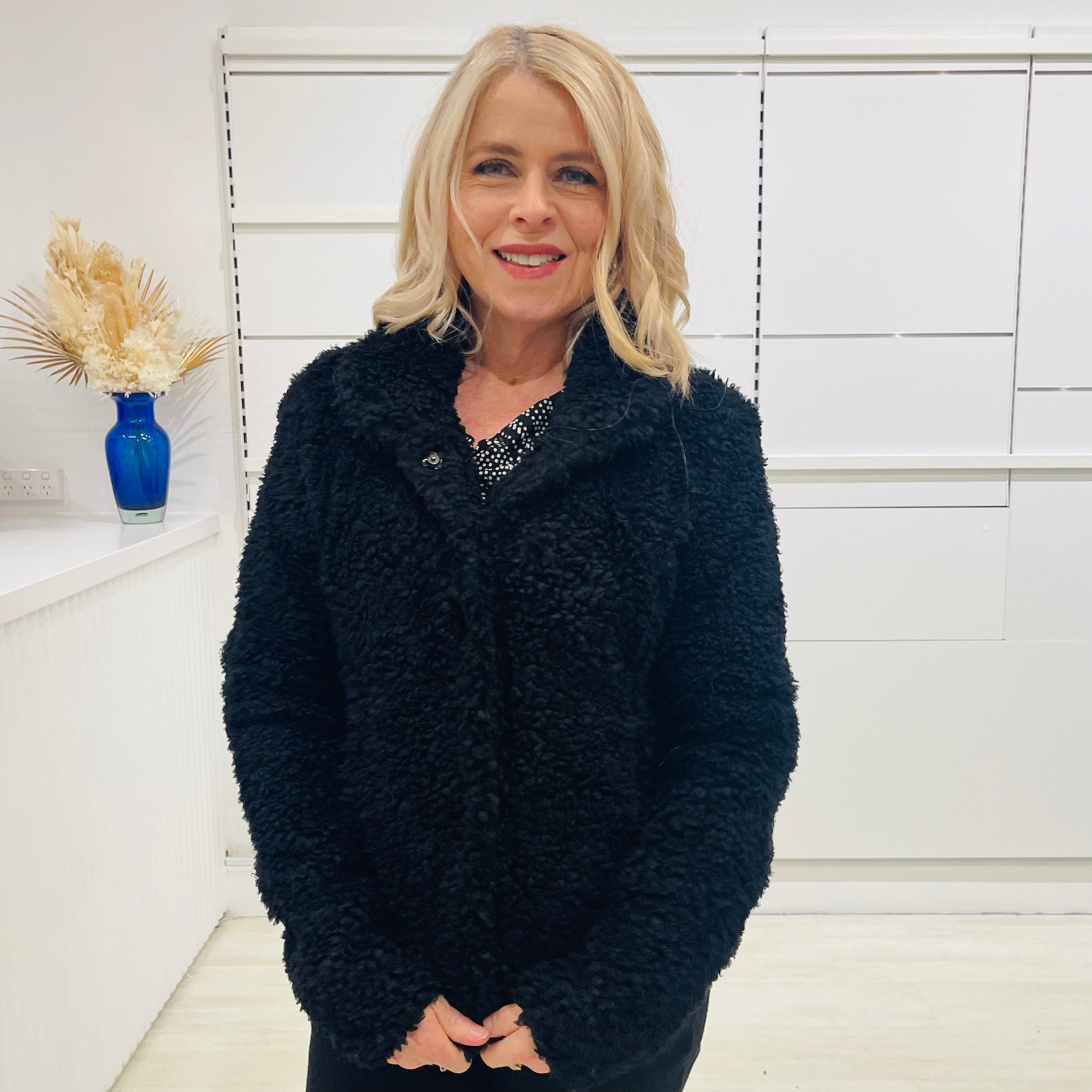 Black fluffy, faux fur, teddy bear jacket with pockets. Worn with black tailored fitted pants and a black and silver sparkly cowl neckline top.