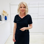 Woman in a black dress standing in a room with white walls and decorative elements.