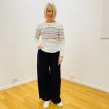 Woman wearing a striped sweater and black pants standing in a room with white walls and wooden floor.