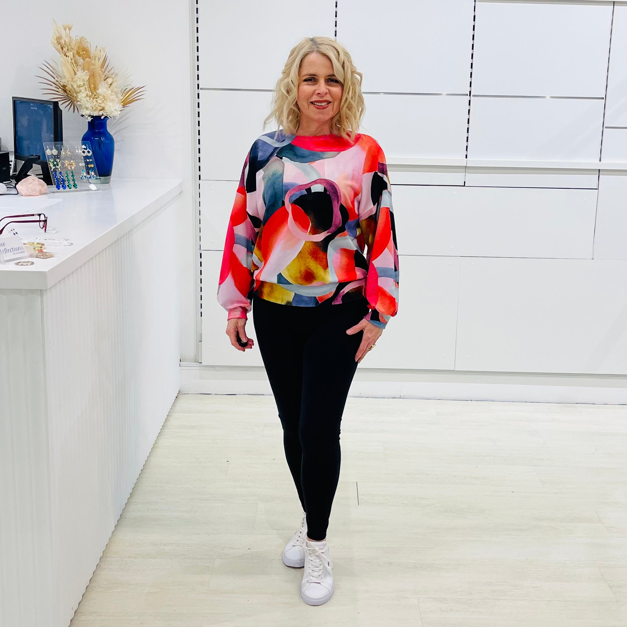 Woman wearing a colorful sweater and black pants in a white photography studio.