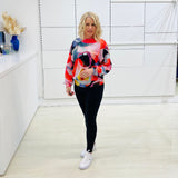 Woman wearing a colorful sweater and black leggings in a white fashion studio.