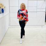 Woman wearing a colorful sweater and black pants in a minimalistic room.