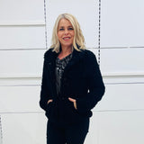 Black fluffy, faux fur, teddy bear jacket with pockets. Worn with black tailored fitted pants and a black and silver sparkly cowl neckline top.