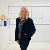 Black fluffy, faux fur, teddy bear jacket with pockets. Worn with black tailored fitted pants and a black and silver sparkly cowl neckline top.