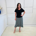 Green,black and white print, stretch, slight a-line skirt, with small ruffle on hemline. Worn with black, cowl neckline, wave sleeve, women's top.