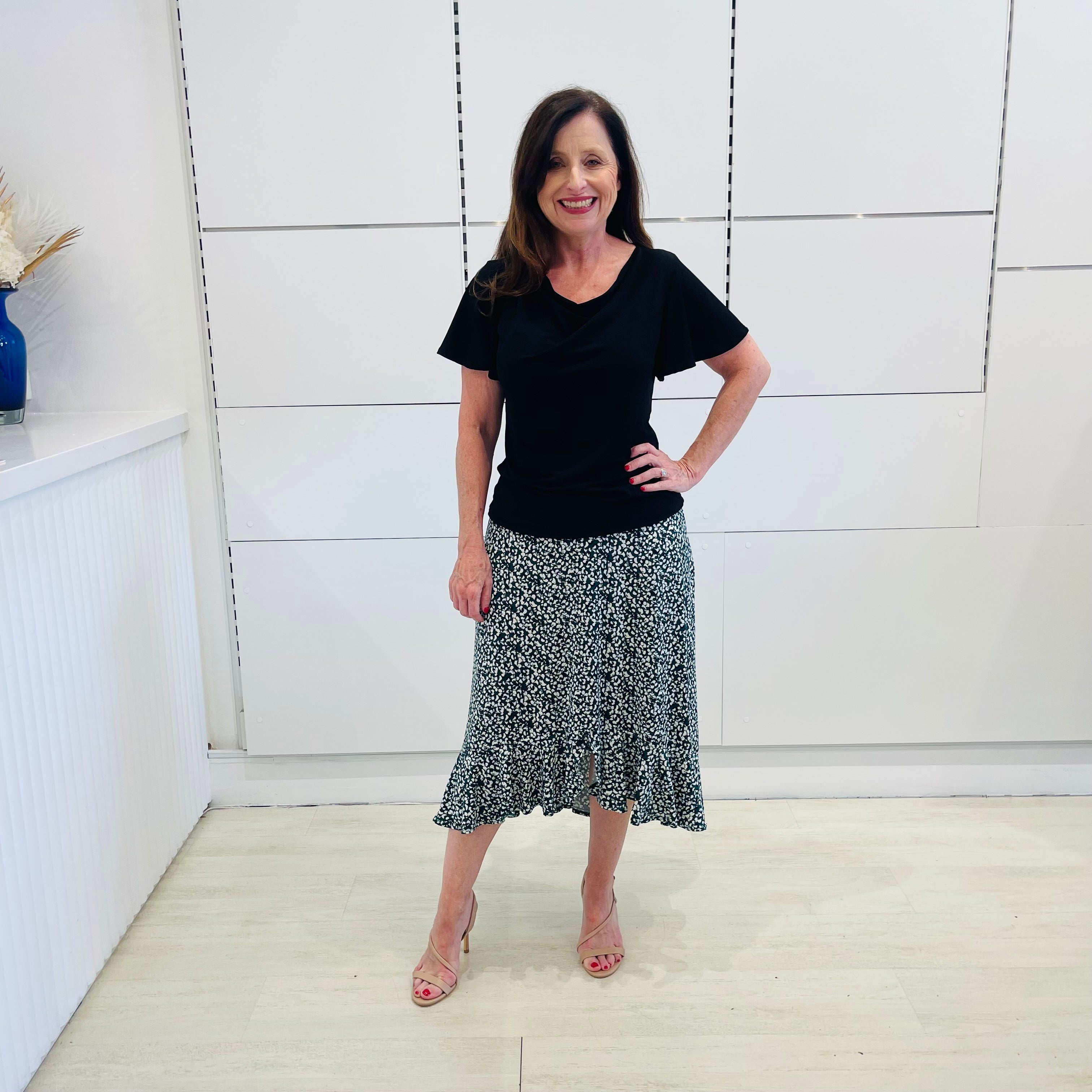 Green,black and white print, stretch, slight a-line skirt, with small ruffle on hemline. Worn with black, cowl neckline, wave sleeve, women's top.