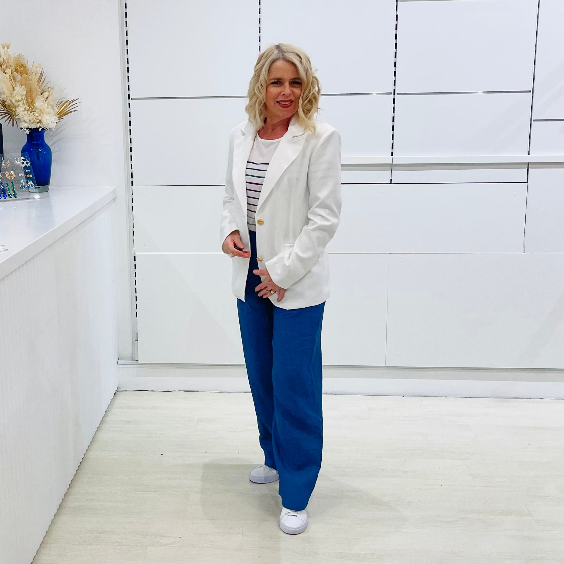 Woman in a white blazer and blue pants standing in a minimalistic room.