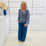 Woman wearing a flowy blue top with long sleeves, a delicate leaf print, paired with denim blue colored linen pants.