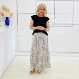 Woman wearing a black top and patterned skirt in a minimalistic room.