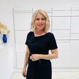 Woman in a black dress standing against a white wall with decorative elements.