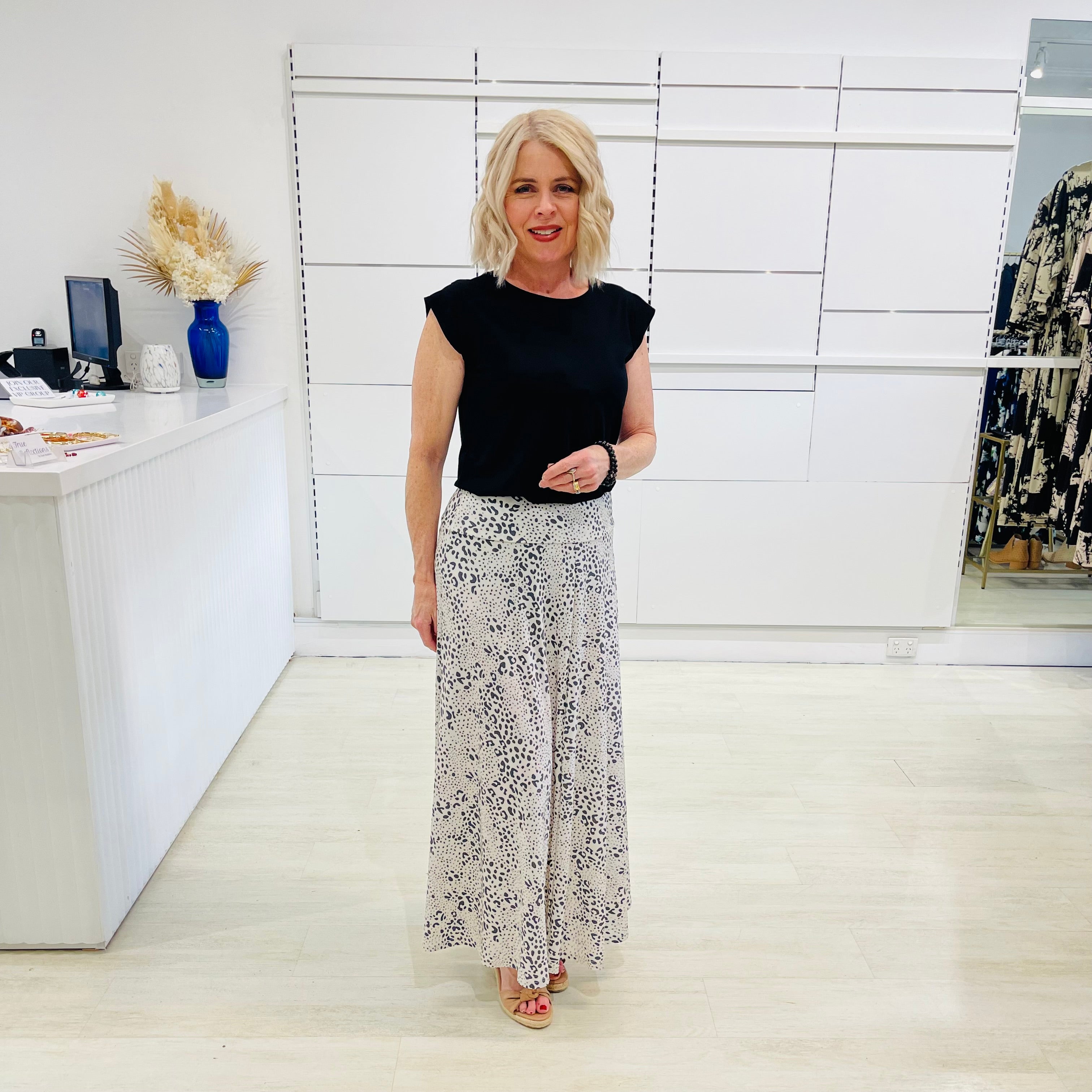 Woman in black top and patterned pants standing in a white room with decor elements.