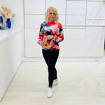 Woman wearing a colorful sweater and black leggings in a white room.
