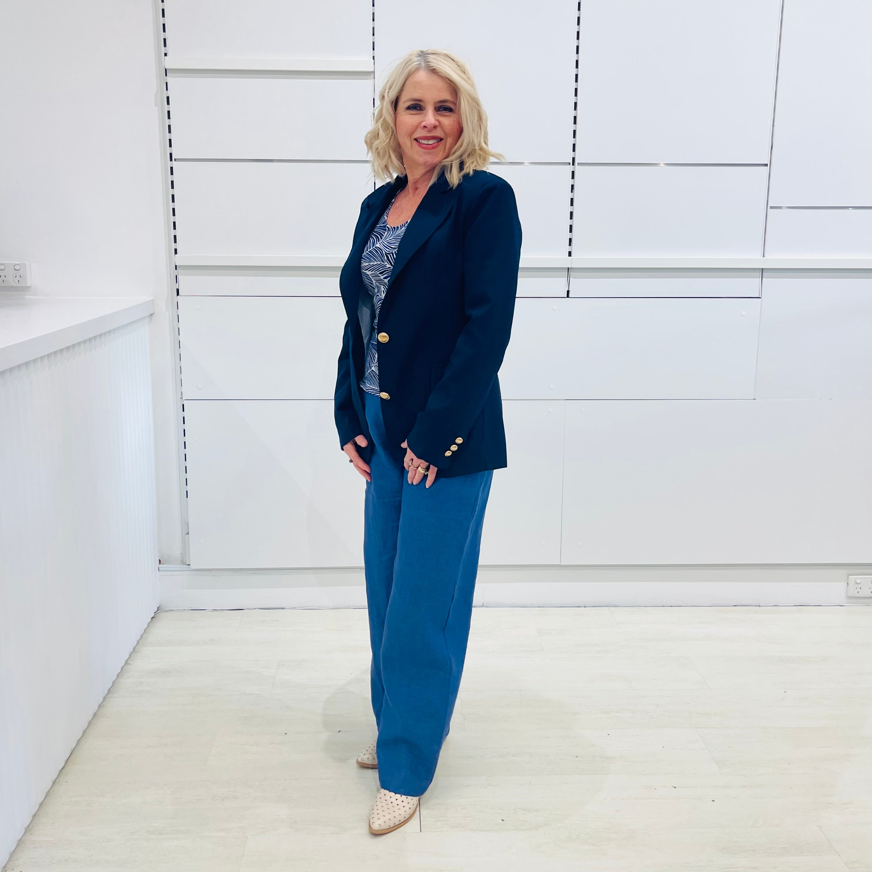 Single breasted, navy blazer for women, with gold buttons. Worn with blue top and blue linen pants.