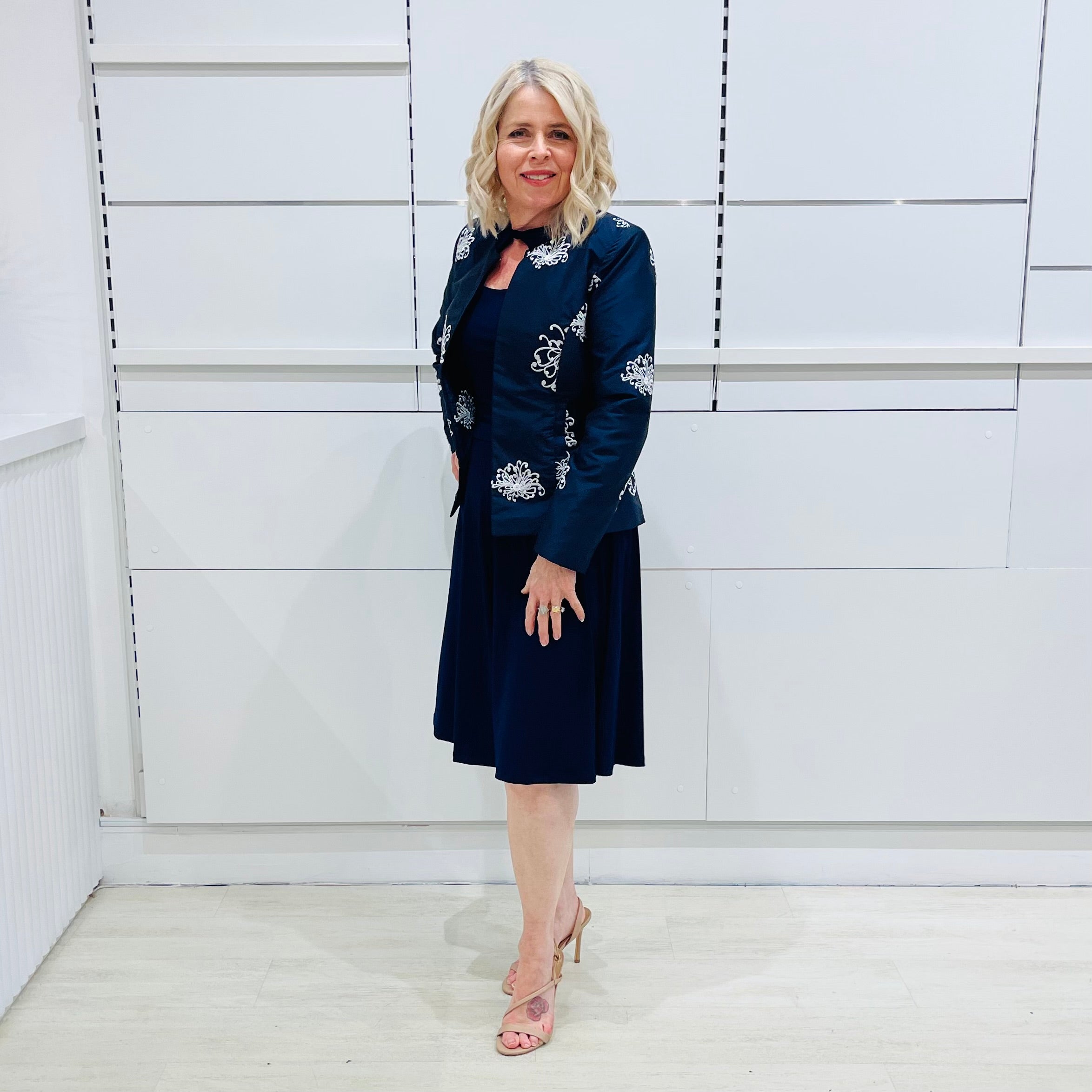 Penelope dress in deep navy blue, worn by model- elegant long sleeve design, knee length, with modern neckline, worn with Navy blue & white embroidered silk jacket, designed and Made in Australia.