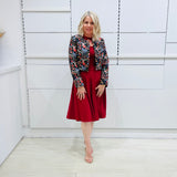 Woman wearing the Penelope dress n rich ruby red, featuring a fit-and-flare, knee length, slihouette, full length sleeves, and a cut out neckline. With embroidered silk bolero Selena Jacket.