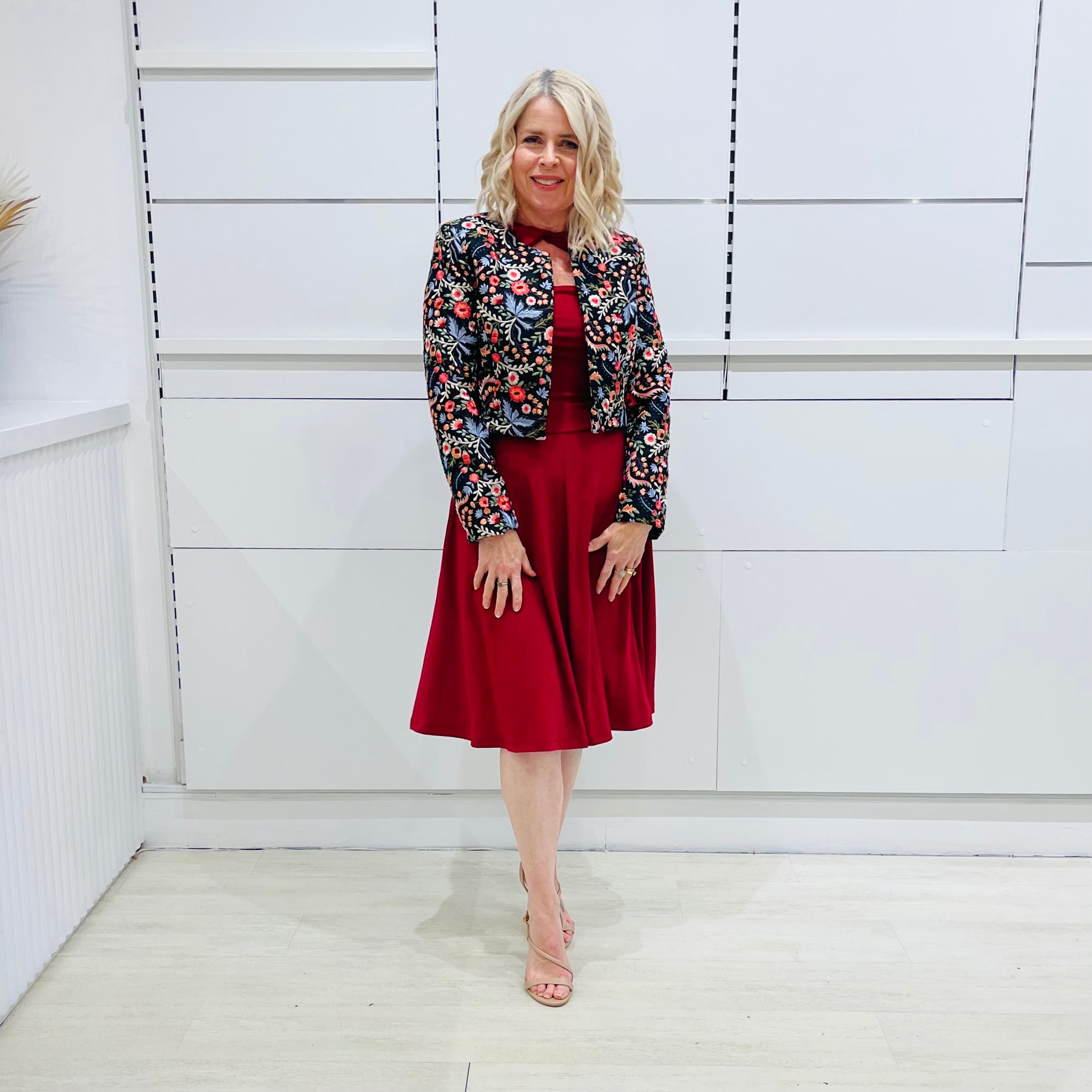 Woman wearing the Penelope dress n rich ruby red, featuring a fit-and-flare, knee length, slihouette, full length sleeves, and a cut out neckline. With embroidered silk bolero Selena Jacket.