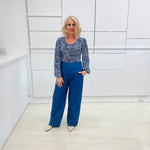 Woman wearing a flowy blue top with a delicate leaf print, scoop neckline, long gathered sleeves, paired with denim blue colored linen pants.