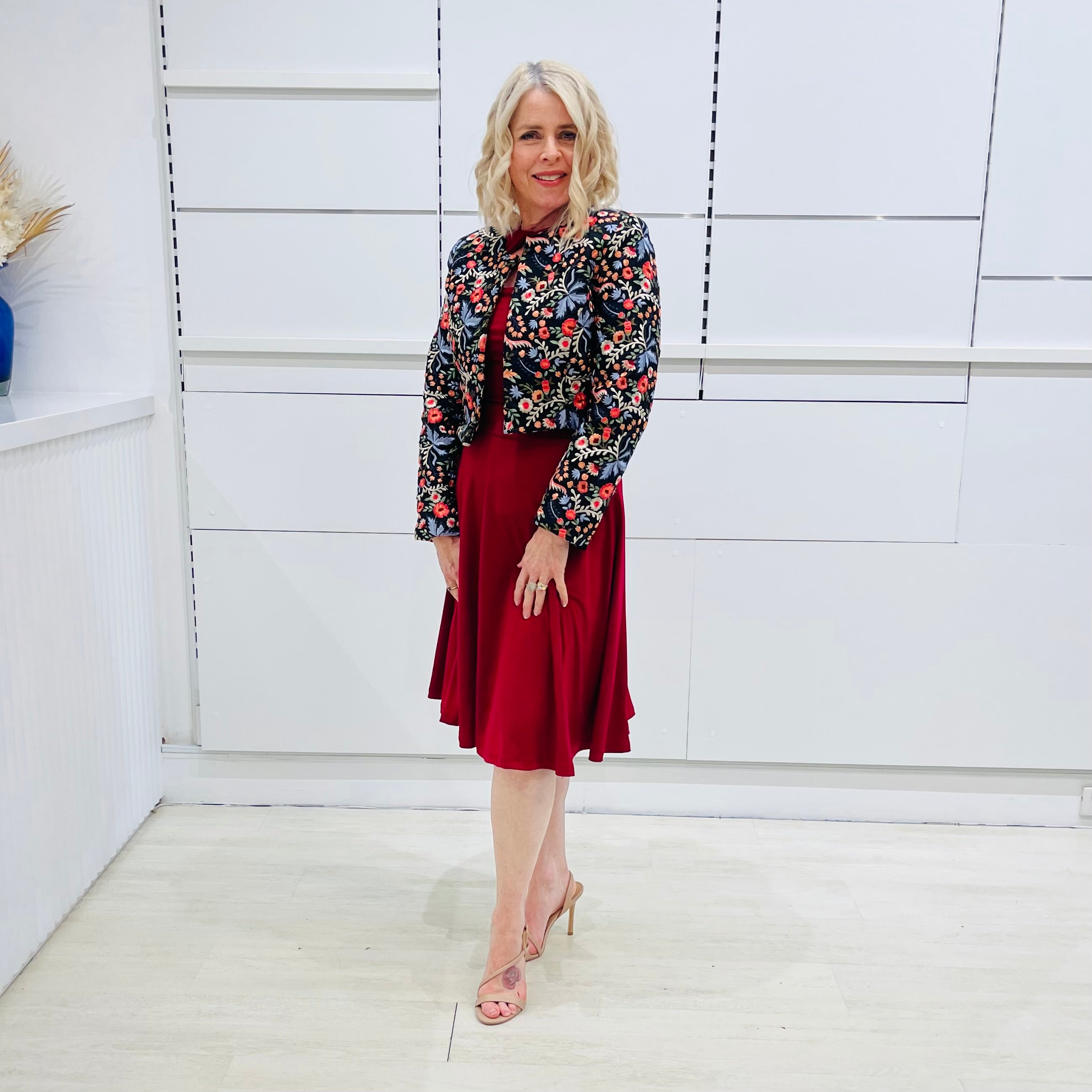 Woman wearing the Penelope dress n rich ruby red, featuring a fit-and-flare, knee length, slihouette, full length sleeves, and a cut out neckline. With embroidered silk bolero Selena Jacket.