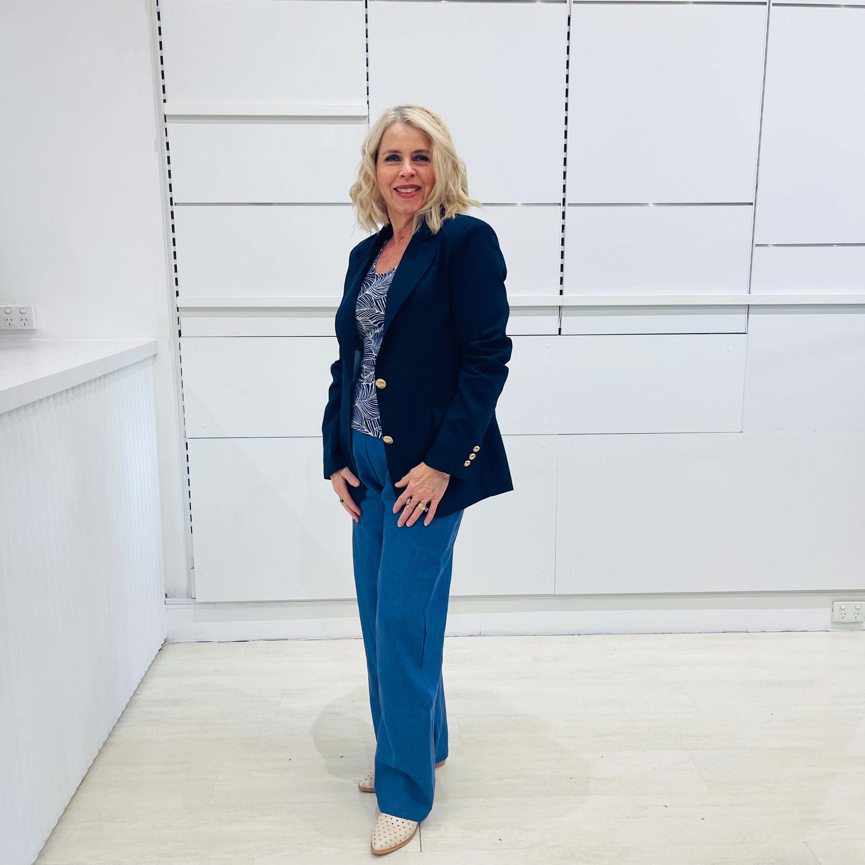 Single breasted, navy blazer for women, with gold buttons. Worn with blue top and blue linen pants.