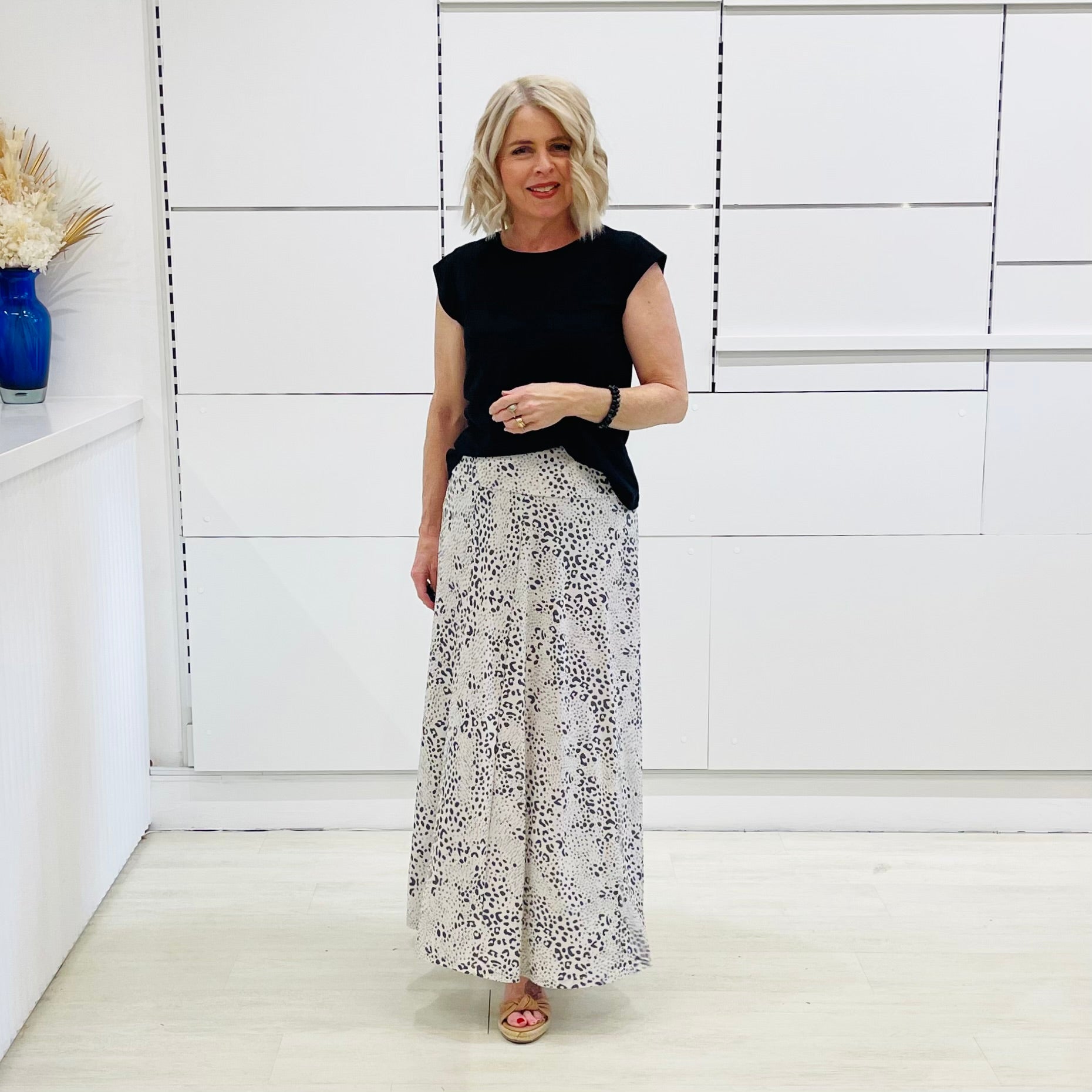 Woman wearing a black top and patterned white skirt standing in a minimalistic room.