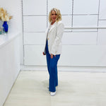 Woman in a white blazer and blue pants standing in a minimalistic room.