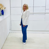Woman in a white blazer and blue pants standing in a minimalistic room.