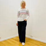 Woman wearing a striped sweater and black pants standing in a room with white walls and wooden floor.