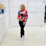 Woman wearing a colorful sweater and black leggings in a white room.