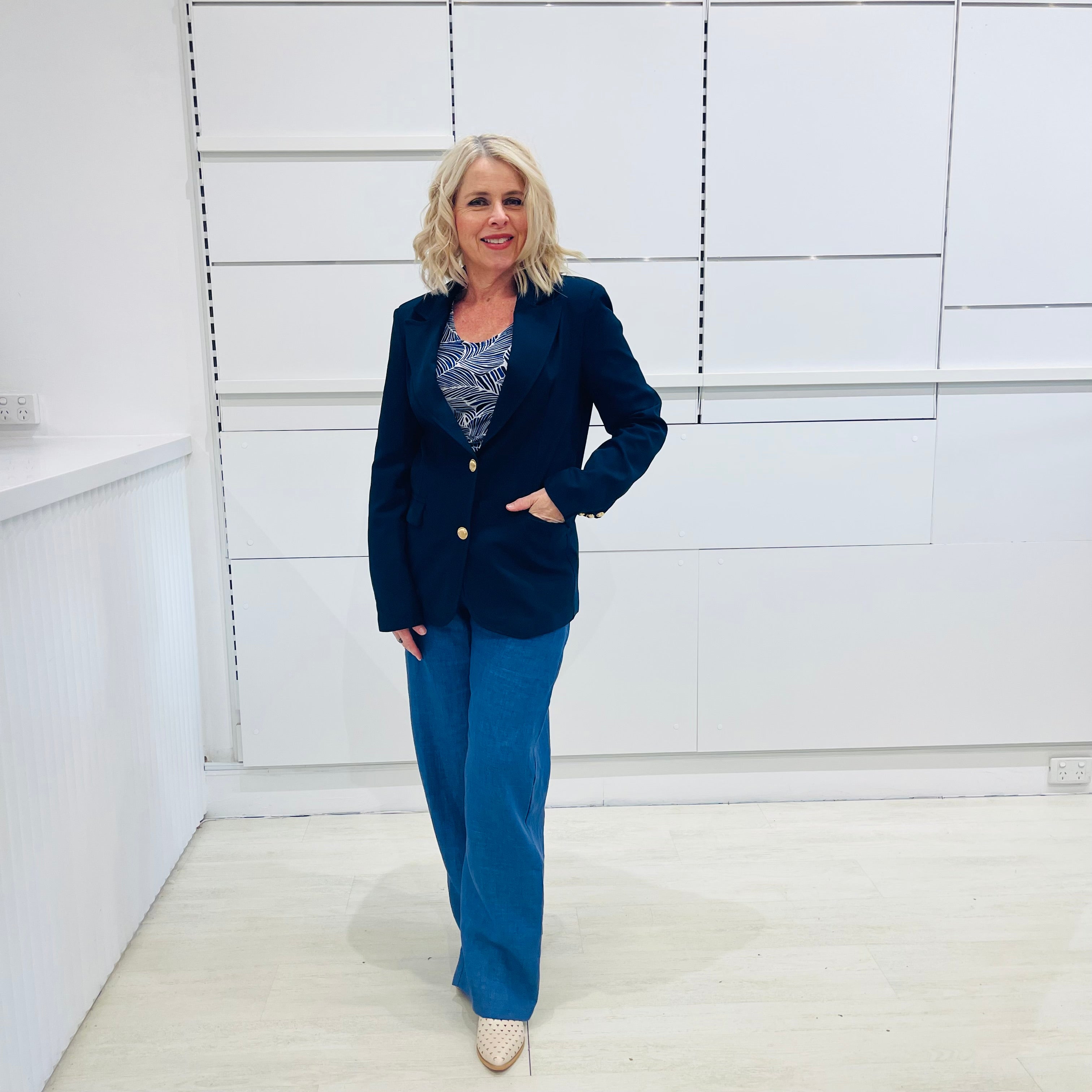 Single breasted, navy blazer for women, with gold buttons. Worn with blue top and blue linen pants.
