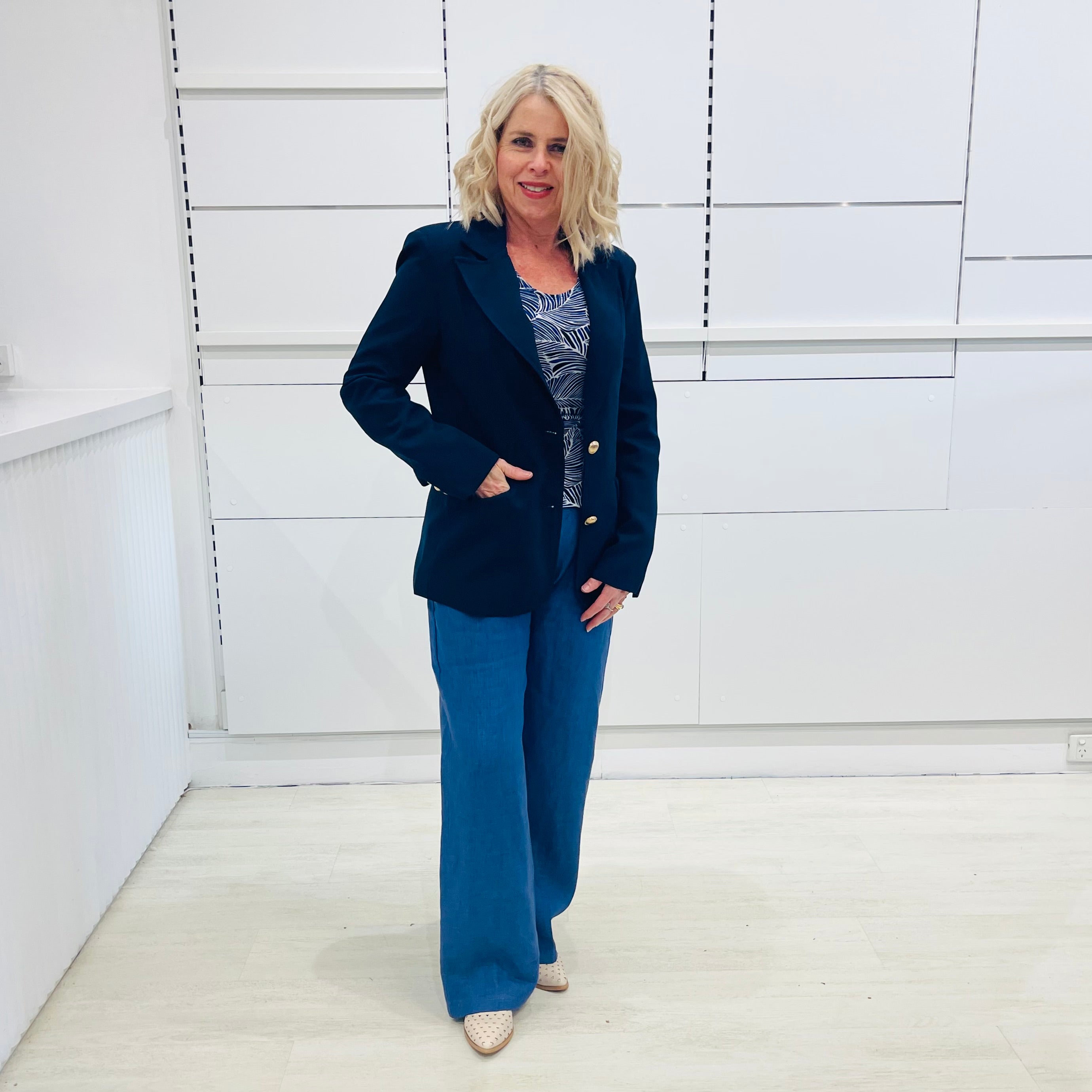 Single breasted, navy blazer for women, with gold buttons. Worn with blue top and blue linen pants.