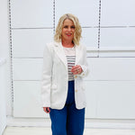 Woman wearing a white blazer over a striped shirt with blue pants against a white background