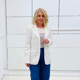 Woman wearing a white blazer over a striped shirt with blue pants against a white background