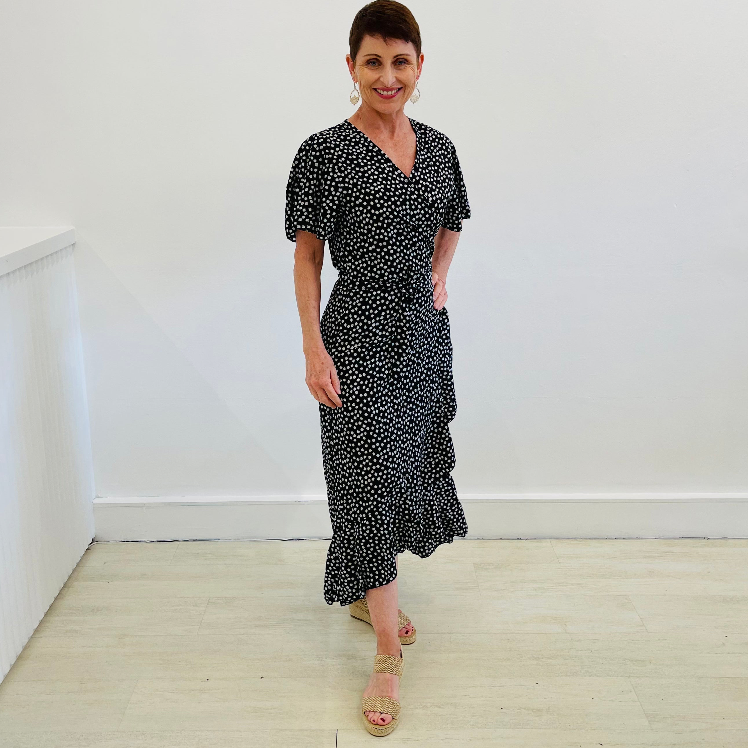 Black with white floral print, wrap around dress, with short airy sleeves, and slight ruffle hemline.