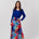 A woman modeling a long-sleeve wrap-style maxi dress with a vibrant blue bodice and a multicolor abstract watercolor print skirt, standing against a light gray studio background.