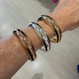 Hand wearing three gold and silver bangles on a light wooden surface.