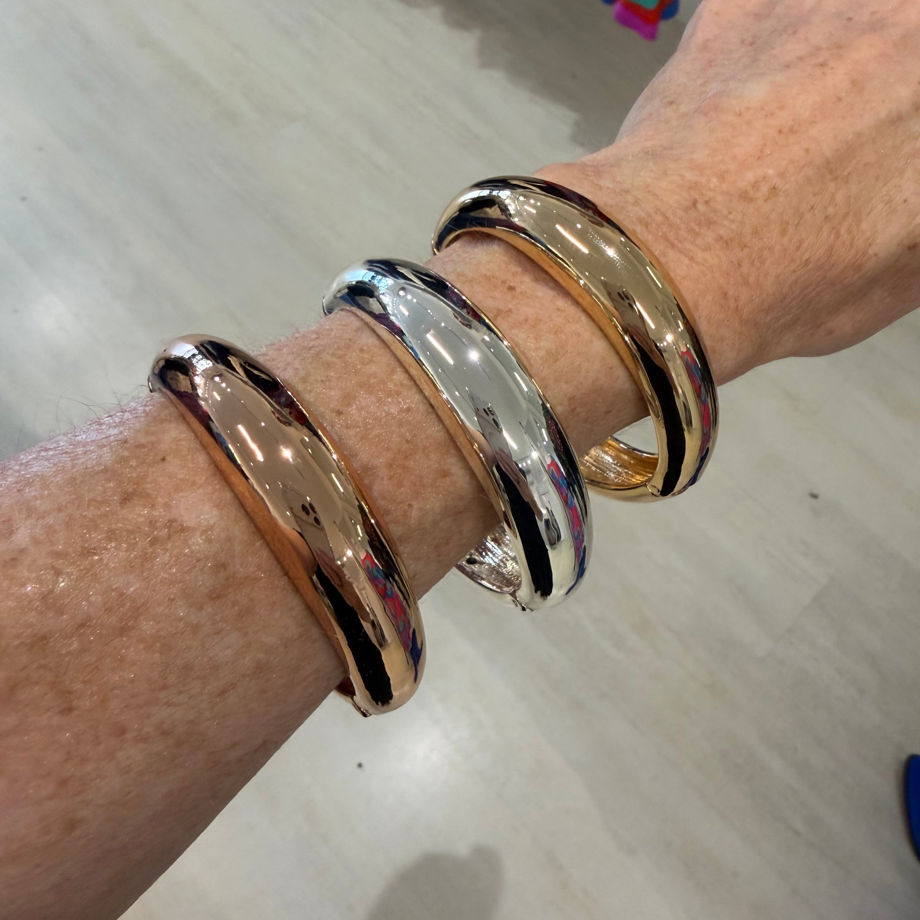 Hand wearing three gold and silver bangles on a light wooden surface.
