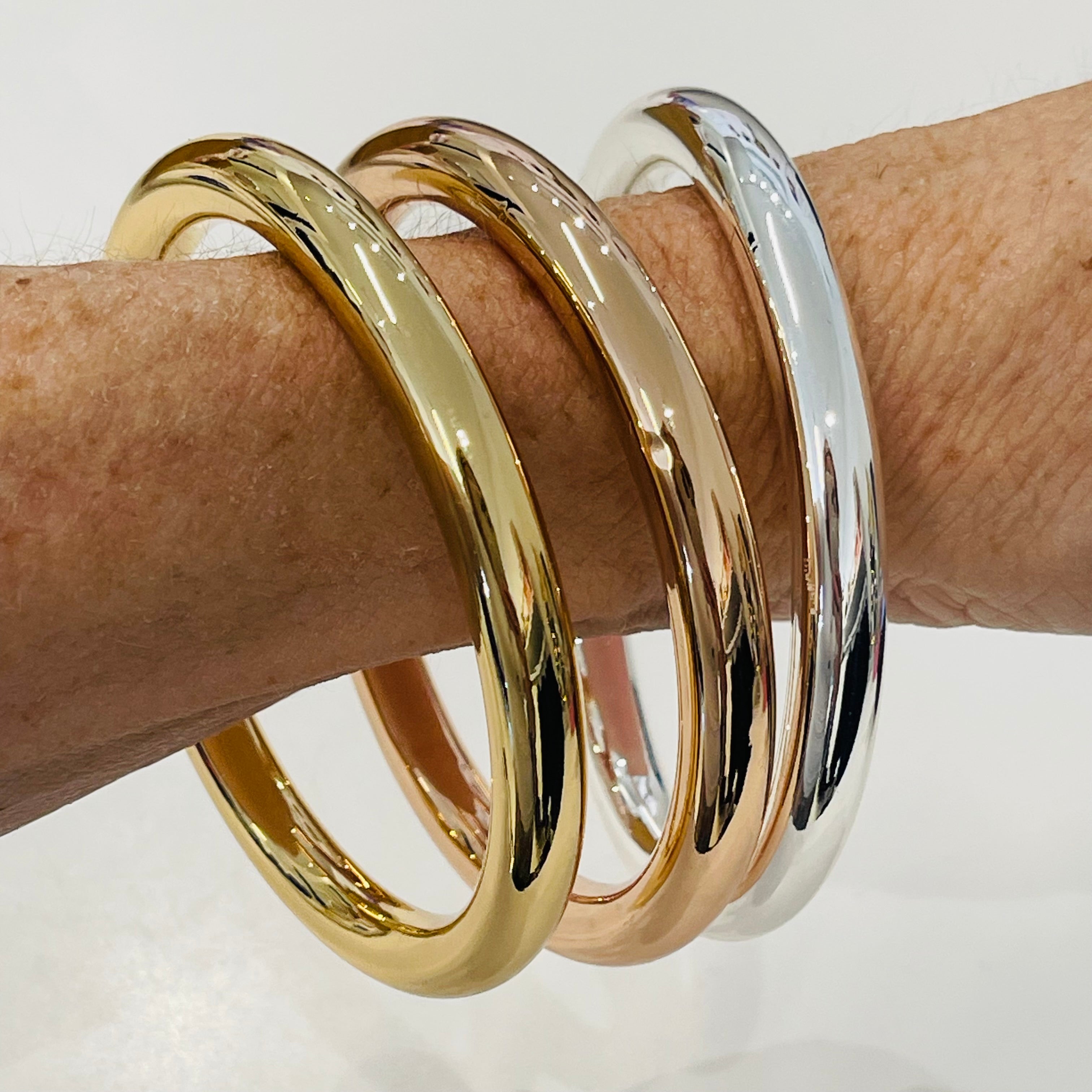 Three gold and silver bangles on a wrist against a white background